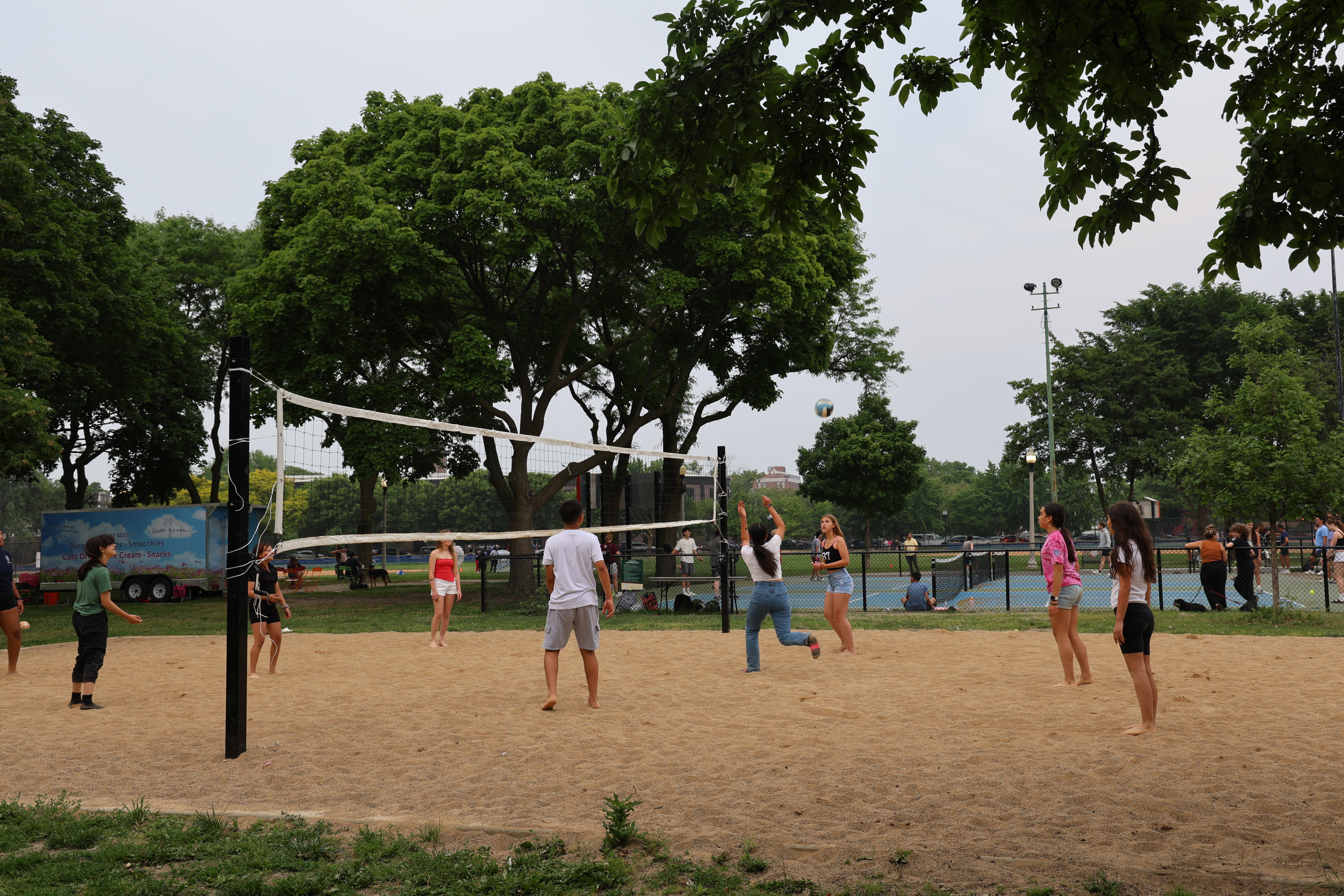 People play beach volleyball on a sand court in a park.